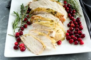 Close-up of sliced herb-butter roasted turkey breast fanned on a white plate with cranberry sauce spooned alongside and fresh thyme garnish, warm candlelight in the background