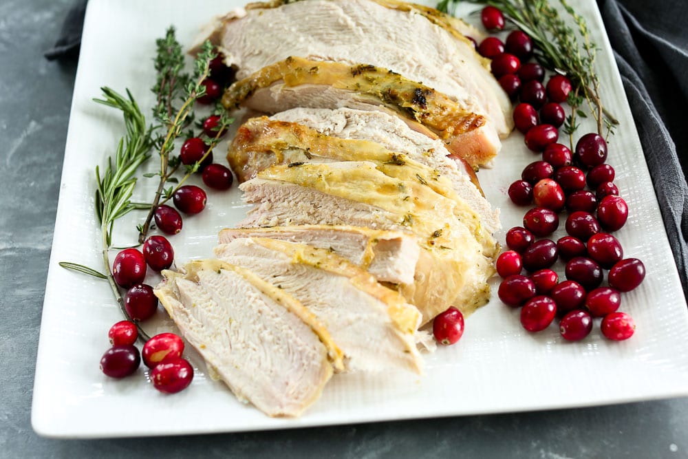 Close-up of sliced herb-butter roasted turkey breast fanned on a white plate with cranberry sauce spooned alongside and fresh thyme garnish, warm candlelight in the background
