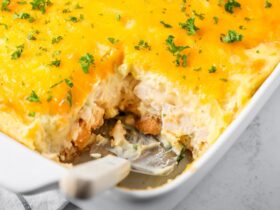 Golden-topped Thanksgiving leftover casserole in a white baking dish with layers of mashed potatoes, stuffing, and turkey visible at the edges, served on a wooden table with a sprig of fresh thyme