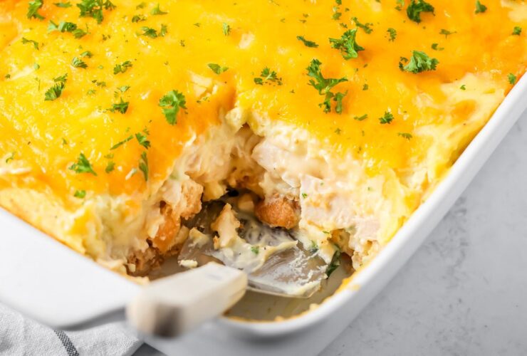 Golden-topped Thanksgiving leftover casserole in a white baking dish with layers of mashed potatoes, stuffing, and turkey visible at the edges, served on a wooden table with a sprig of fresh thyme